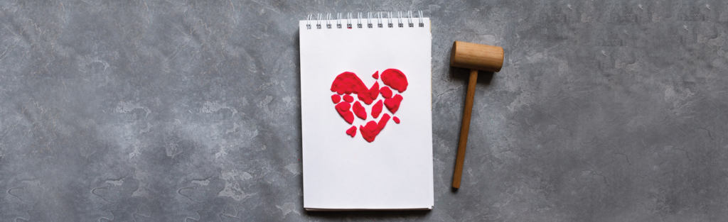 A white notepad sits on a grey table top with a shattered red heart and a wooden gavel off to the side. 